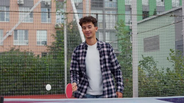 Young smiling man enjoying playing table tennis outdoors