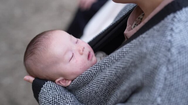 Close view of a sleeping baby resting against an adult in a woven fabric carrier.