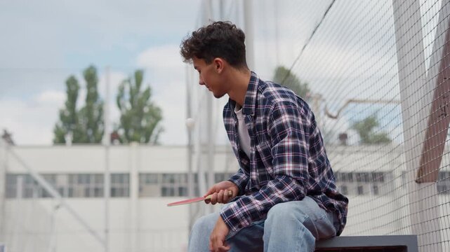 Young man bouncing a table tennis ball on a racket outdoors