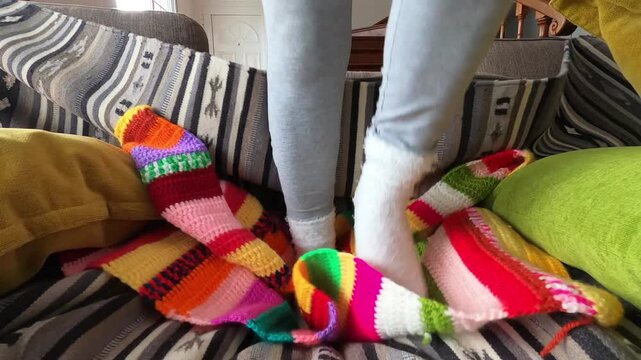 A person's socked feet playfully bounce and stomp on a vibrant, multi-colored crochet blanket, bringing a sense of cozy energy and joyful movement to a comfortable home setting.