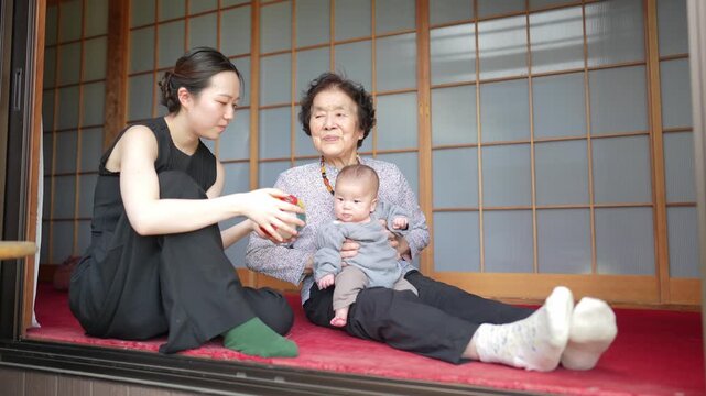 Younger woman holds a colorful patchwork ball while sitting beside an older woman holding a baby.