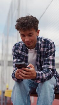 Young smiling man texting on a smartphone at the sports court