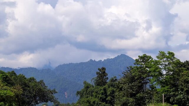 A scenic view of lush forest-covered mountains beneath layers of soft, dramatic clouds.