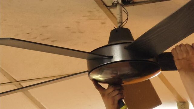 Slow motion close up of technician hands installing a dark ceiling fan with a screwdriver.
