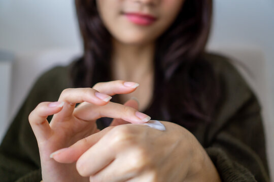 Close up of woman applying cream to hand with fingers. Attractive woman gently massaging moisturizer into her hands during a calming self-care routine at home.