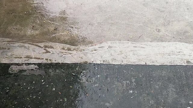 Concrete floor shows dry wet transition line as rain spreads, textured ground surface with contrast during weather change.