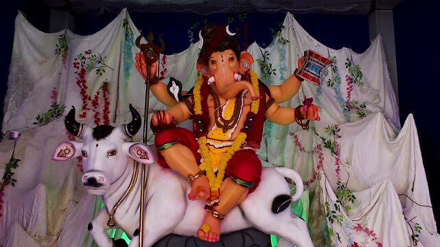 Ganesha idol dressed as Shiva seated on white Nandi bull, trishul and damru in hand, white drape decoration Ganesh Chaturthi India.