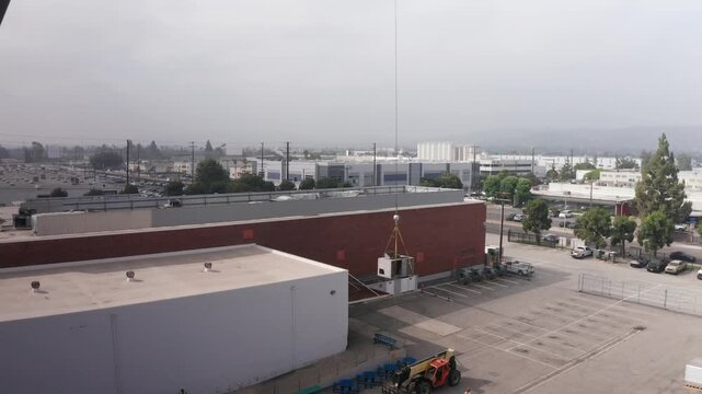 Aerial wide pullback shot of a construction crane operating at a commercial site for HVAC replacement during gloomy weather in Baldwin Park, California. 4K