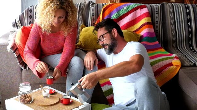 A lovely couple enjoys a cozy morning at home, relaxing on the sofa. The man pours fresh coffee into cups, sharing warm drinks and a pleasant conversation. They embrace a moment of domestic happiness.