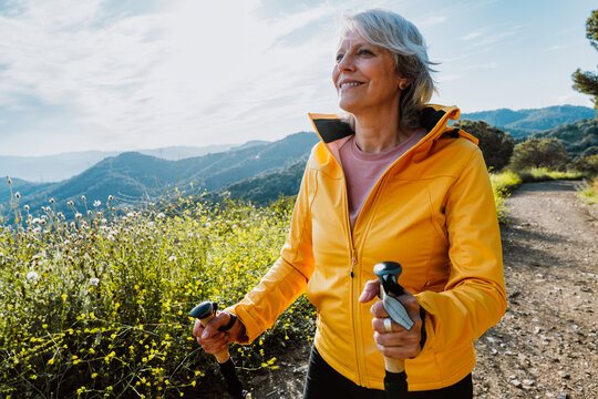 Active senior woman hiking on outdoor trail using trekking poles
