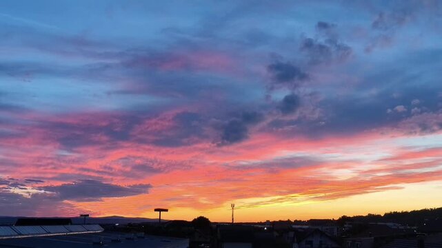 Time lapse of a vivid pink and orange sunset sky with clouds moving over a small town skyline at dusk, colorful dramatic evening cloudscape, beautiful nature background, fast motion