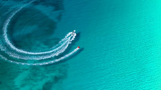 Aerial drone view shows a boat creating curved white wake patterns across clear turquoise water. Dark underwater areas contrast with the bright Caribbean Sea in Riviera Maya Mexico