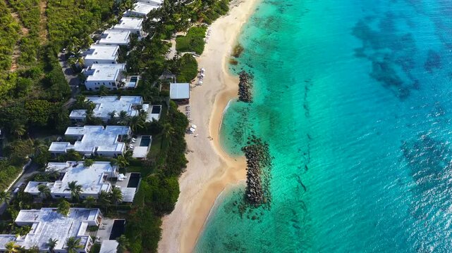 Aerial drone view shows white sandy beach beside turquoise Caribbean water and coastal buildings. Rocky barriers extend into the sea along Riviera Maya Mexico