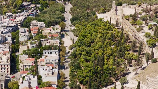 Stunning aerial footage showing the ancient Odeon of Herodes Atticus and the Dionysiou Areopagitou street, revealing the historic cityscape and lush greenery of Athens, Greece
