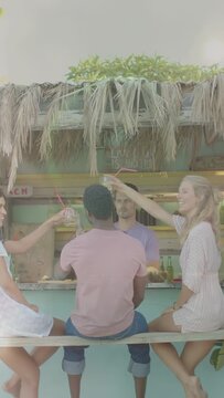 Vertical video: Women reaching red straws tapping man's head, lifting drinks toasting at beach bar