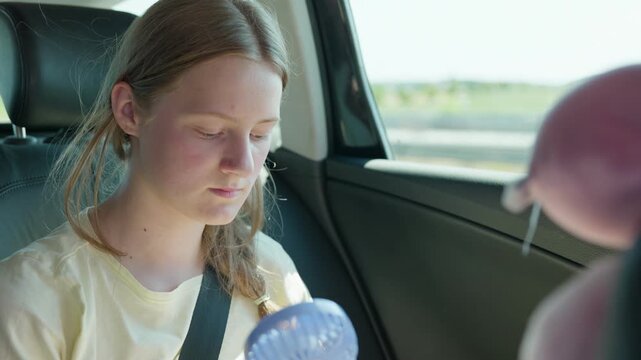 Girl with a handheld fan in a car slow motion a trip on a hot summer day