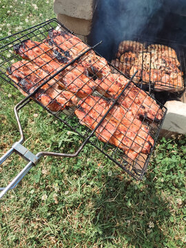 Juicy meat steaks grilling on wire grate over open brick fire pit for outdoor summer barbecue and family picnic concept