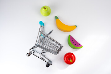 Shopping cart with colorful toy fruits, representing healthy choices, consumerism, and grocery shopping for kids © Alberto