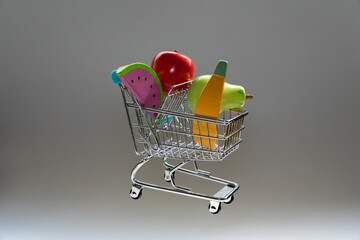 Miniature shopping cart filled with wooden toy fruit, symbolizing retail, consumerism, and childhood play © Alberto