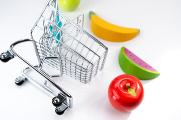 Miniature shopping cart with wooden toy fruits, representing grocery shopping, consumerism, and retail concepts © Alberto