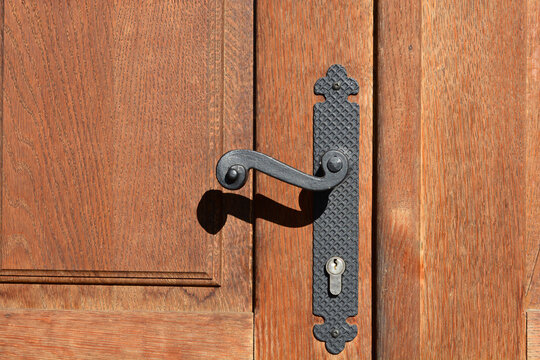 A close up shot of a black antique wrought iron handle and backplate mounted on a traditional brown wooden door pane.