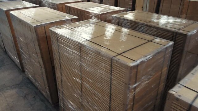 Stacks of wrapped wooden panels and plywood boards stored on pallets in industrial warehouse   