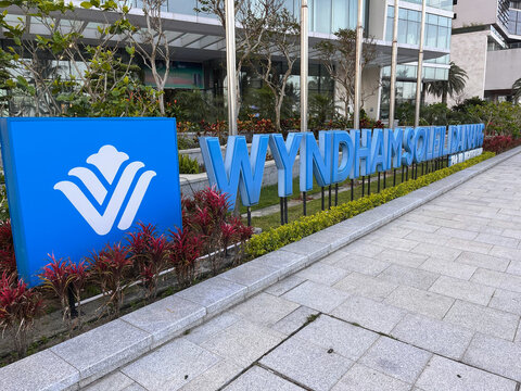 A large blue sign displays the name 'WYNDHAM' in bold letters. The sign is set against a modern architectural backdrop. Surrounding greenery enhances the urban landscape.