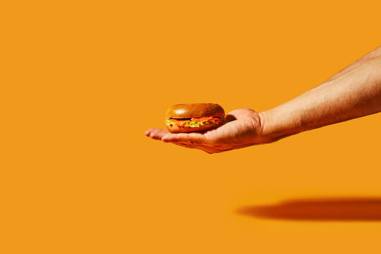 Hand Holding a Fresh Salmon Bagel Sandwich on Vibrant Orange Background