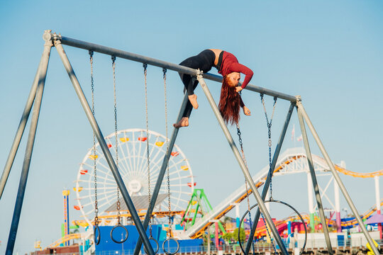 White woman hanging upside down on swing set with amusement park rides