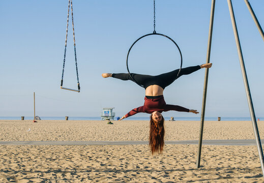 White woman performing split on aerial hoop at California beach