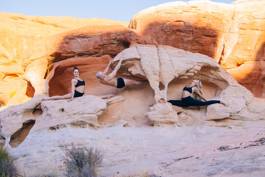 Three white people practicing yoga and acrobatics on desert rock