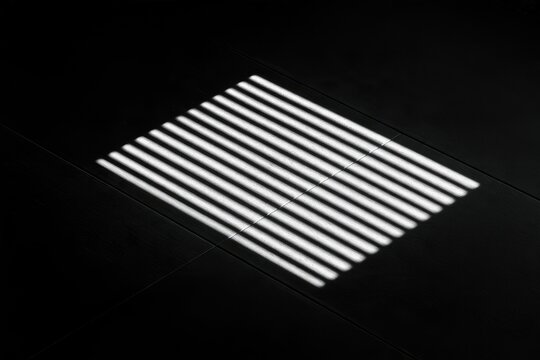Stark parallel light bars cast a crisp shadow on a dark, textured surface