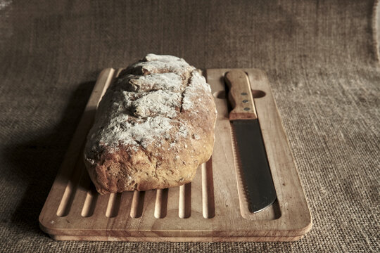 Rustic sourdough bread on wooden board with knife showing organic grain texture and natural wellness mood in a simple artisan scene.