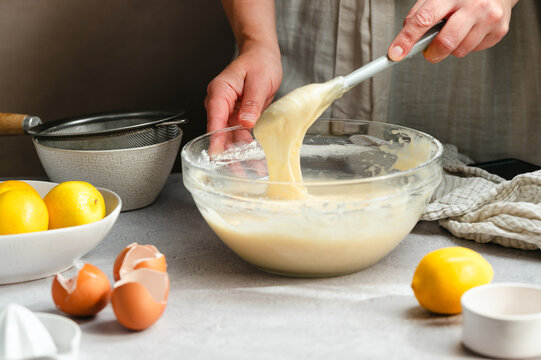 Woman whisking lemon cake batter in a glass bowl, process of cooking a lemon cake