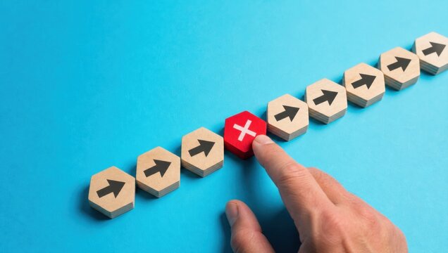 supply chain management logistics risk management. Hand pressing a red wooden block with a white cross interrupting a row of blocks with black arrows on blue background.