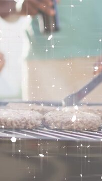 Vertical video: Hand flipping burgers with tongs on grill cooking evenly, pal spraying oil, sparkle