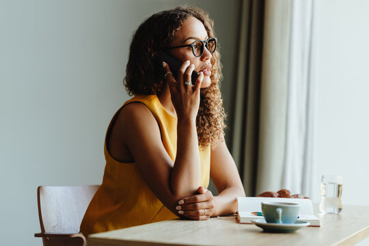 Woman in cafe talking on cellphone with notebook and coffee