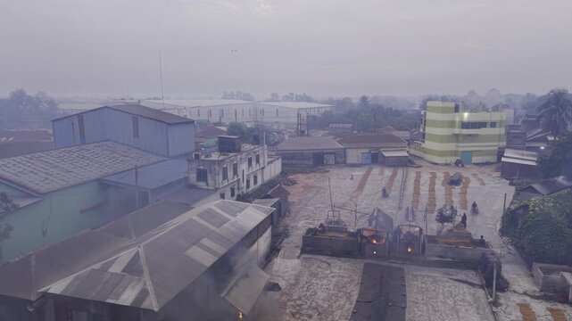Orbiting drone footage captures workers beginning manual paddy handling at a Khajanagar rice mill, showing the drying yard and early morning rice processing activity from multiple angles.
