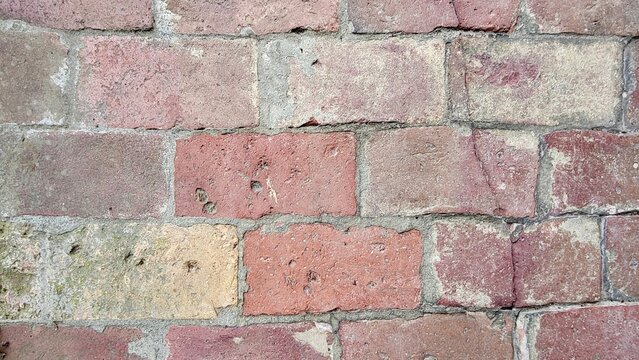Close-up of an old weathered brick wall displaying subtle pastel pink and gray tones. The aged bricks, irregular surface and delicate color variations create an authentic architectural texture.