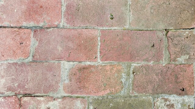 Close-up of an old weathered brick wall displaying subtle pastel pink and gray tones. The aged bricks, irregular surface and delicate color variations create an authentic architectural texture.