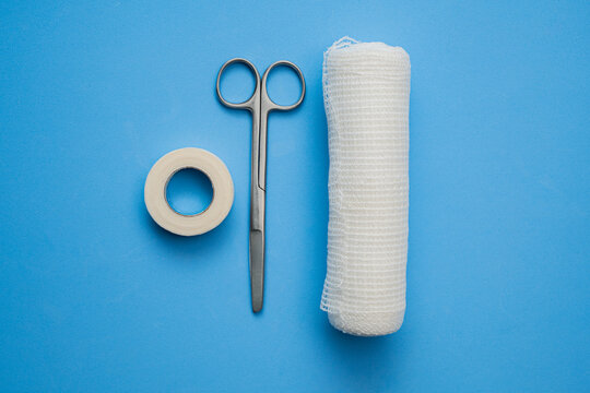 First aid supplies including medical scissors, gauze bandage, and adhesive tape on a blue background for wound care