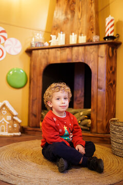 Boy celebrating Christmas sitting on a rug with a festive sweater and decorated fireplace background