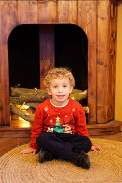 Young boy smiling, sitting in front of fireplace, wearing festive Christmas sweater, celebrating holiday season
