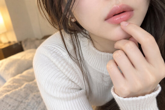 白いニットを着て下唇へ人差し指を添える女性の口元