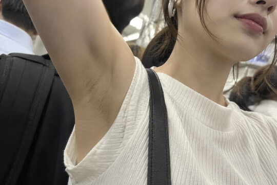 混雑した車内で腕を上げる白いリブの服の女性の接写