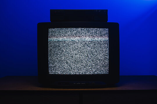 Retro CRT television with VCR displaying analog static interference in dark room with blue lighting