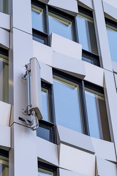 White modern facade with windows and security camera, showing contemporary building surfaces through geometric cladding around the camera and windows
