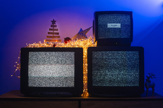 Vintage CRT televisions showing static among glowing holiday lights and decorations