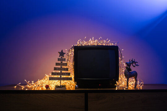 Vintage CRT television with blank screen surrounded by glowing Christmas lights and festive holiday decorations