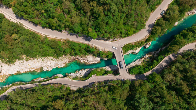 Aerial top down perspective captures turquoise Soca river crystal clear water. Simple bridge crosses rocky canyon banks surrounded by dense wild green forest near Kobarid.